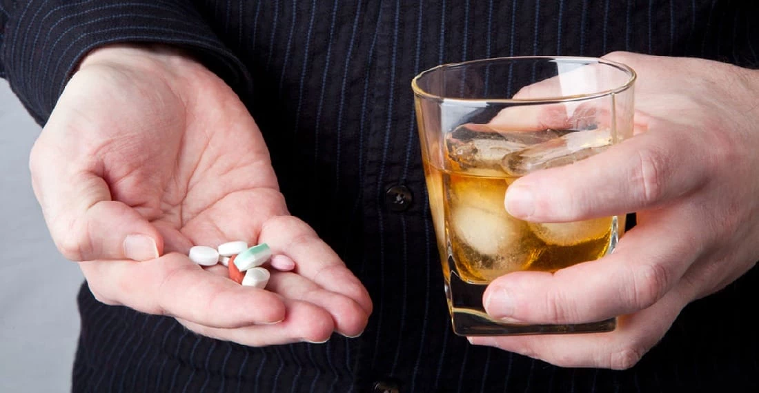 Мужчина с таблетками и стаканом алкоголя в руках